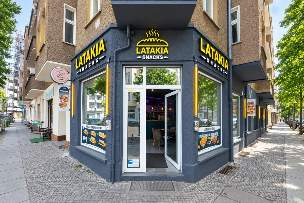 LATAKIA SNACKS – Eckfassade mit Beschriftung und Fenstergrafiken.